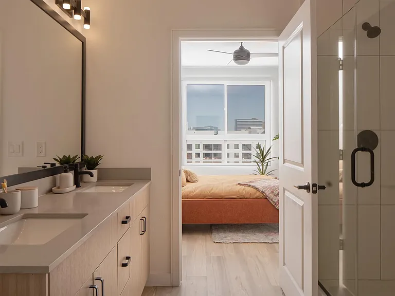 Dual sinks, matte black fixtures, and a glass-enclosed shower create a clean, connected bath that flows seamlessly into the bedroom.