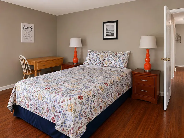 Well-appointed bedroom with hardwood floors, a full bed, nightstands with lamps, and a work desk for studying or WFH.
