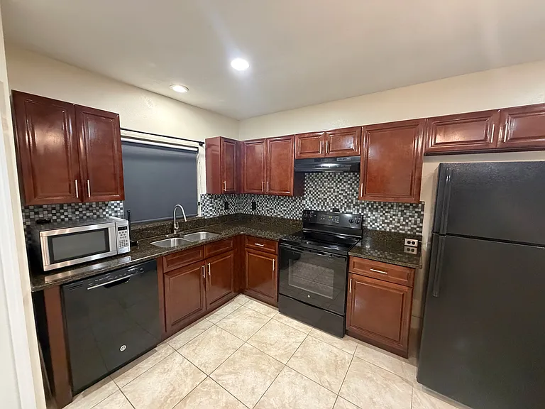 The kitchen boasts solid wood cabinetry, a complete set of appliances, and dark granite countertops.
