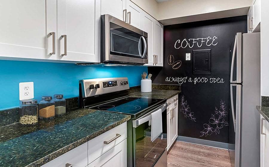 Newly renovated Finish Package III kitchen with new white cabinetry, granite countertops, stainless steel appliances, painted backsplash, chalkboard accent wall, lighting, fixtures, and hard surface flooring