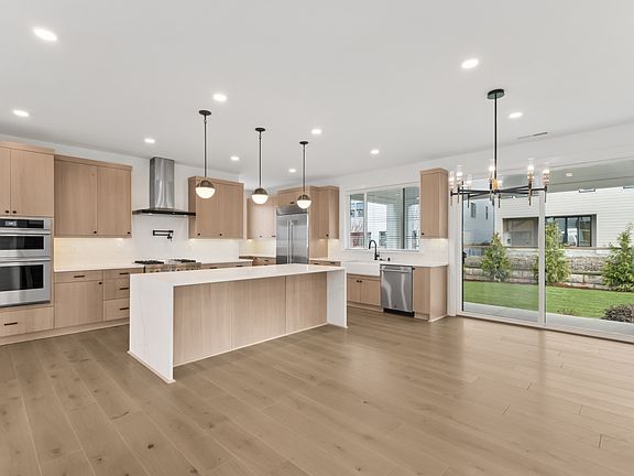 A modern, open-concept kitchen with light wood cabinetry, a large island, and a view of the backyard