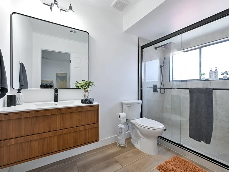 Updated bathroom with large vanity storage, wide mirror, and a glass-enclosed walk-in shower with window.