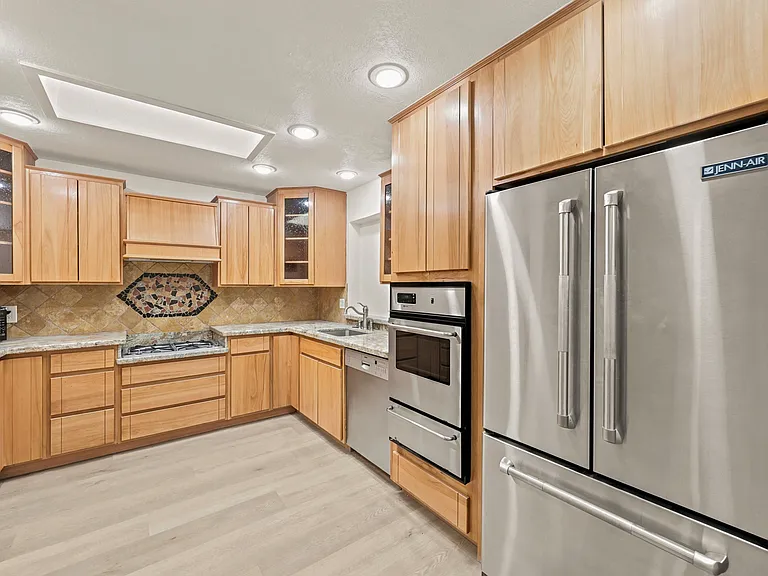 Spacious U-shaped kitchen with ample wood cabinetry, stone-look counters, tile backsplash, and stainless steel appliances.