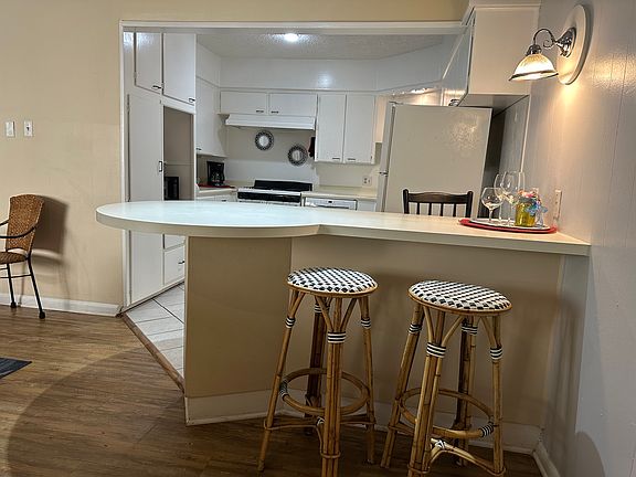 Bright and welcoming living space with two cozy couches, a TV, and a dining area. The open layout flows into a kitchen with abundant storage and a convenient breakfast bar with seating.