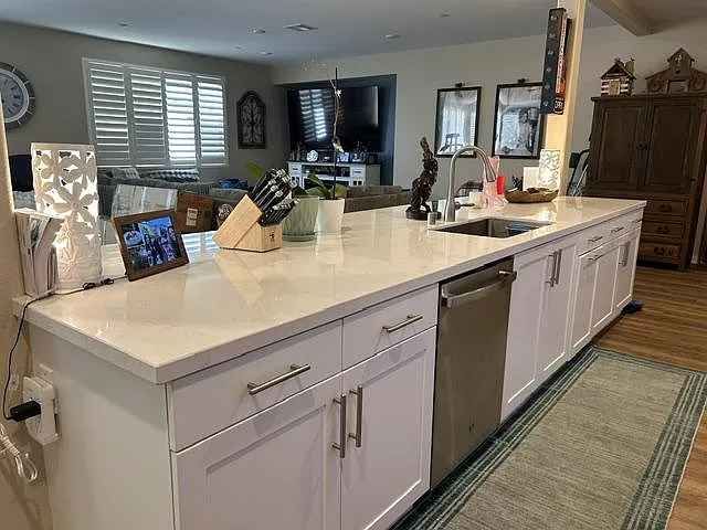 Large kitchen island with quartz counters, undermount sink, dishwasher, and ample cabinet storage for meal prep and gathering