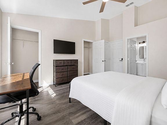 Spacious bedroom with a dedicated desk area, wall-mounted TV, and two closets, plus convenient access to a nearby bath.