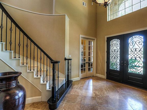 Grand entry way with soaring ceilings, detailed entrance door and wrought iron stair railing.