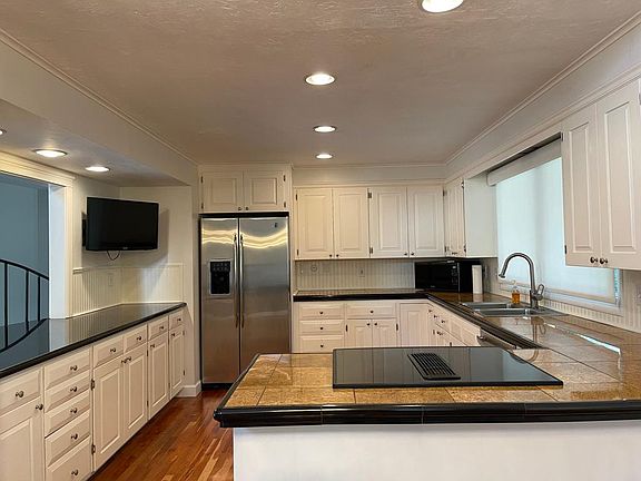 Kitchen with hard wood floors, front-facing new Pella windows with Lutron-controlled roller blind, dishwasher, stove/oven, fridge with ice maker, microwave, and tv on a wall-mount.