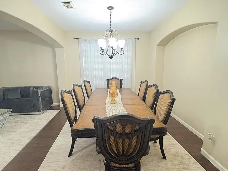 Formal dining area with a full-size table for eight, chandelier lighting, and an arched opening to adjacent living space.