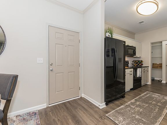 Entry way and kitchen view with black appliances, wood inspired flooring, modern lighting