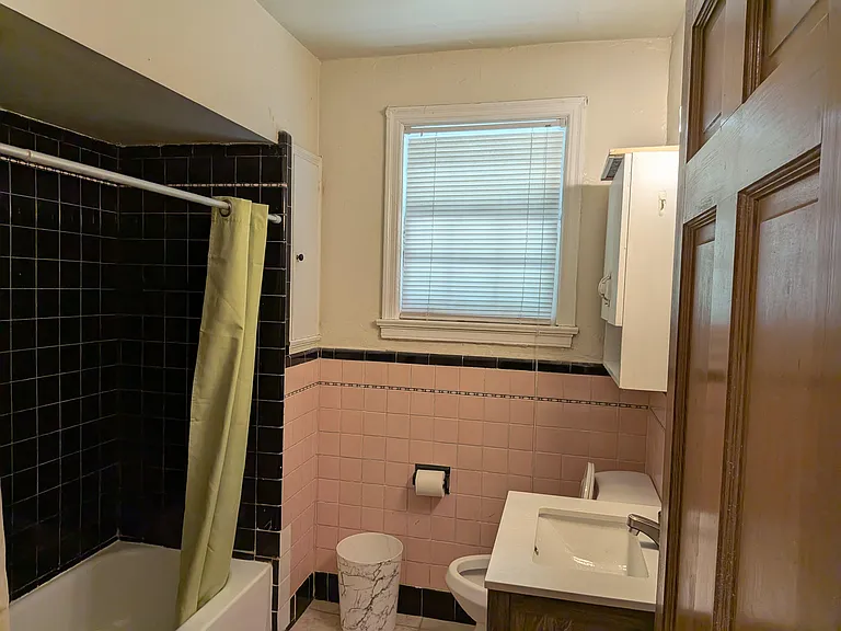 Full bathroom with tiled tub/shower, window with blinds for ventilation, and a vanity sink with wall cabinet storage.