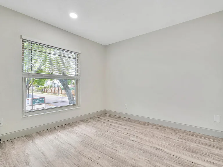 Bright and airy room featuring sleek hardwood flooring, large windows offering a serene view of lush greenery outside.