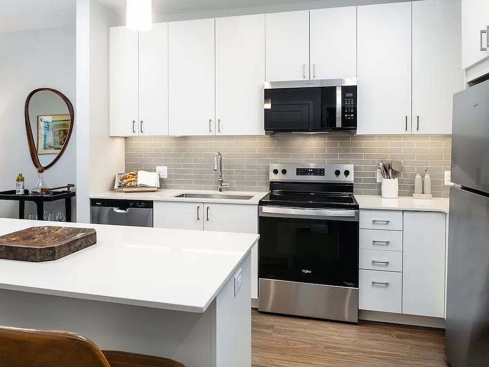 Design Collection I kitchen with stainless steel appliances, white cabinetry, grey tile backsplash, under-cabinet lighting, white quartz countertops, and hard surface flooring