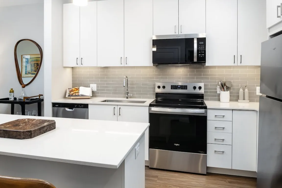 Design Collection I kitchen with stainless steel appliances, white cabinetry, grey tile backsplash, under-cabinet lighting, white quartz countertops, and hard surface flooring