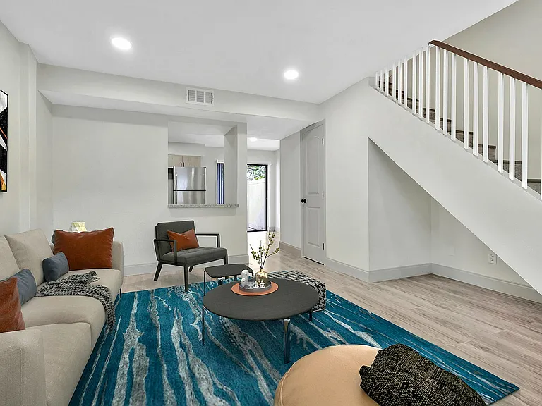 Contemporary living room with elegant staircase, vibrant decor, and an open view to the sleek kitchen.