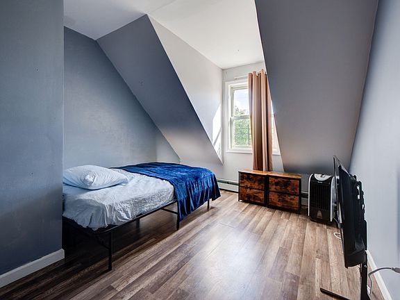 Private bedroom with a sloped ceiling, laminate flooring, window with curtains, and space for a bed and dresser.