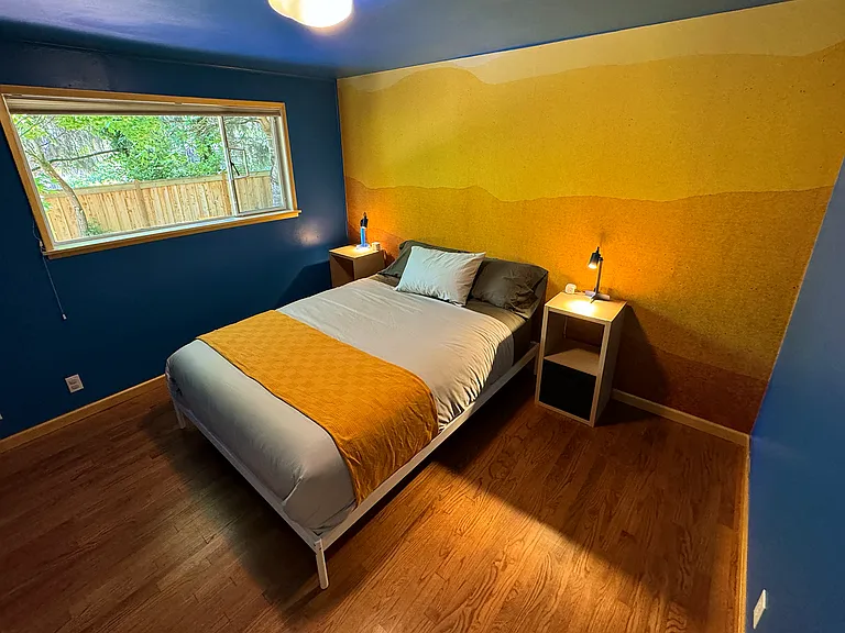 Bedroom 3 furnished with a queen bed, side tables and a closet. It is across from the main bathroom and share the same hallway as bedroom and 2 (currently occupied)