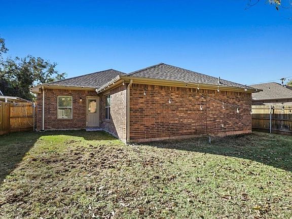 Back of house featuring a fenced backyard, brick siding, and a shingled roof