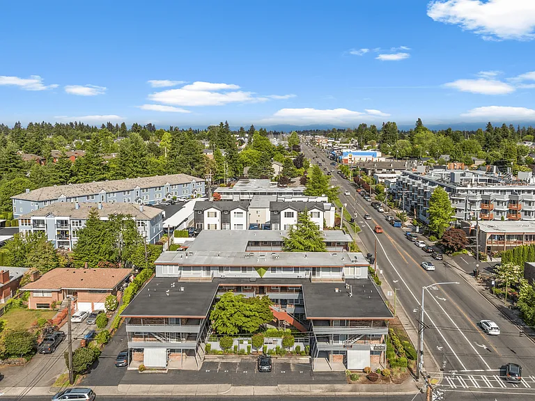 A vibrant suburban neighborhood featuring residential buildings and a busy main street on a sunny day.