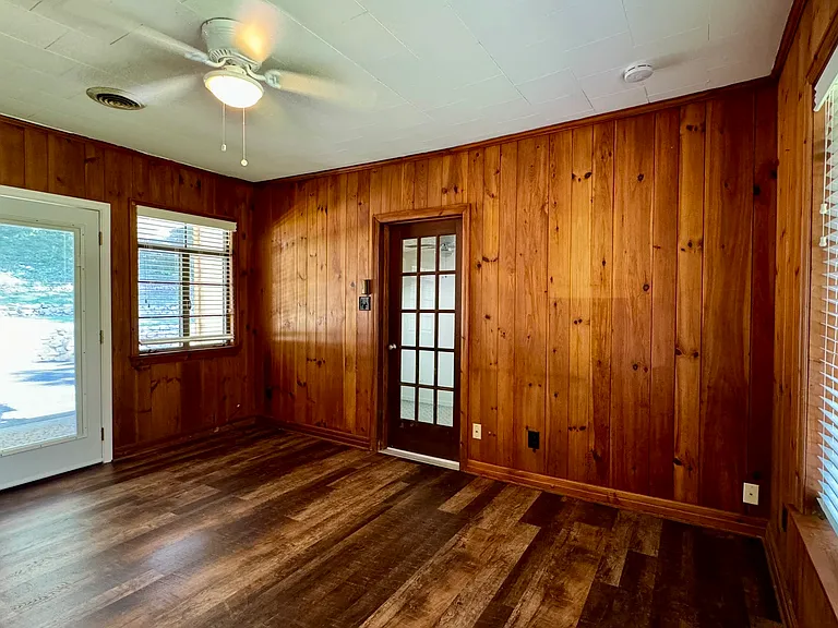 Den with original wood plank walls and new laminate flooring; door to back porch and yard to the left; door to Bedroom 3 at center of photo.