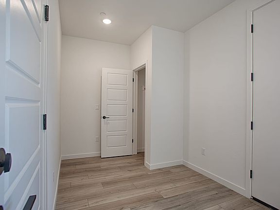A bright, minimalist hallway with white walls, a wooden floor, and several closed doors leading to o