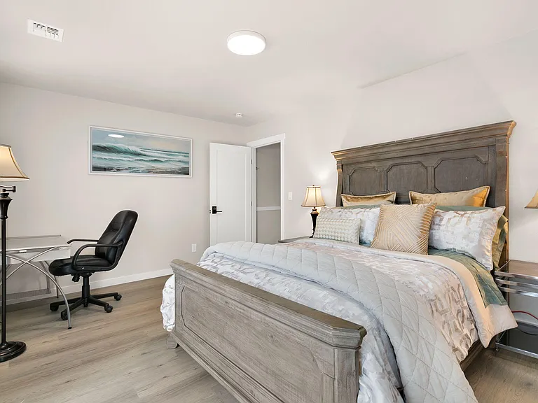 Furnished bedroom with a full bed, matching nightstands and lamps, plus a desk setup for work or study.