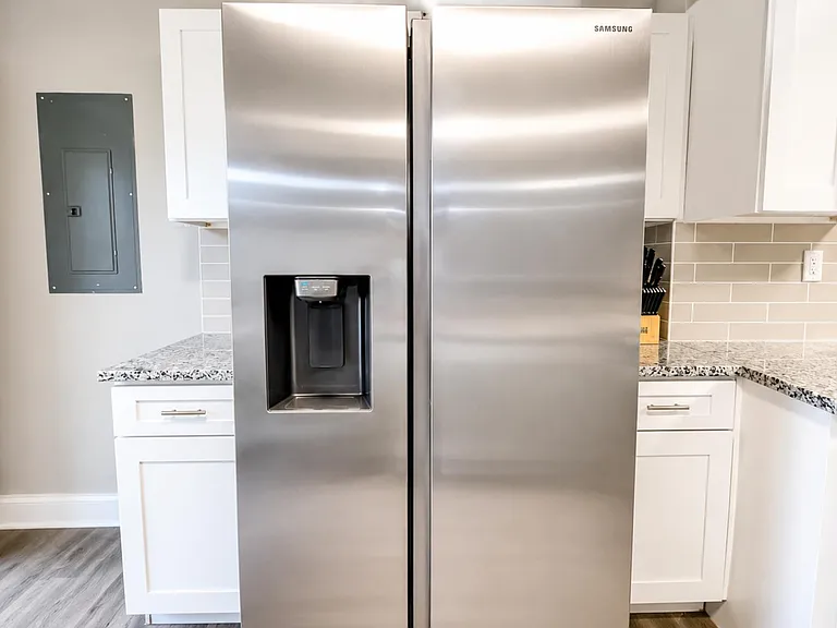 Kitchen features stainless side-by-side refrigerator with in-door dispenser, ample white cabinetry, and stone-look counters.