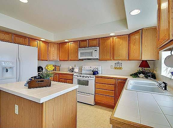 The island kitchen features oak cabinets, tile counters, & a tiled island