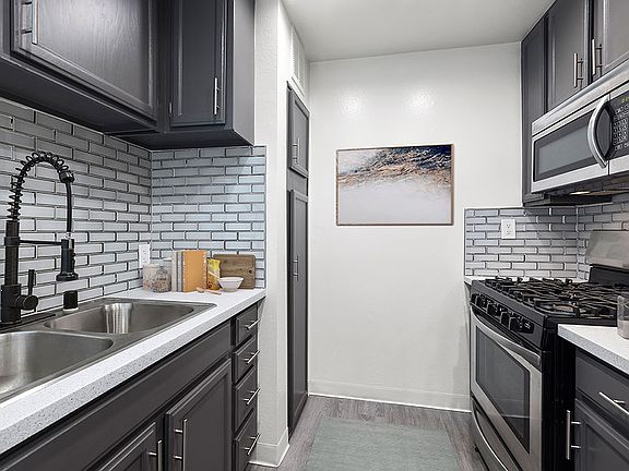 White tiled kitchen with stainless steel fridge, oven, microwave, and fixtures.