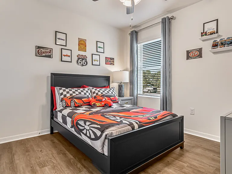 St. Cloud, FL, House Rentals - Ibis Park at Harmony West - Bedroom with Luxury Vinyl Plank Flooring, Bed, Nightstand with Lamp, Wall Decors, Floating Shelves, and Window.