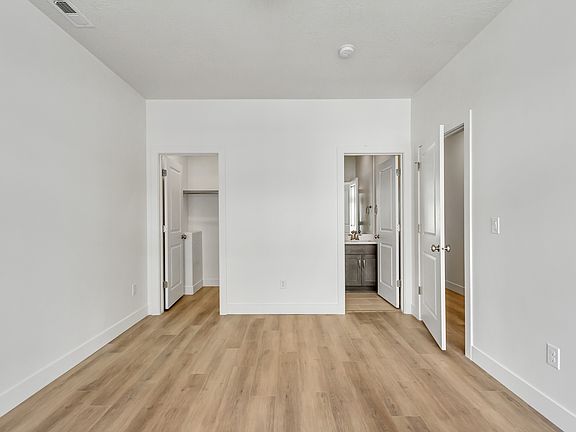 A bright, empty room with light wood flooring, two open doors on the left to a closet and bathroom,
