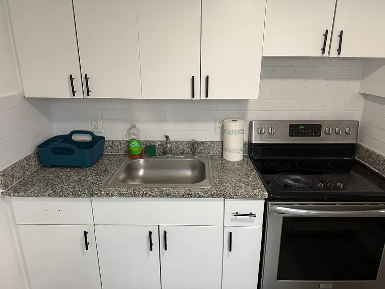Functional kitchen workspace with ample white cabinetry, subway-tile backsplash, granite-look counters, and an electric range