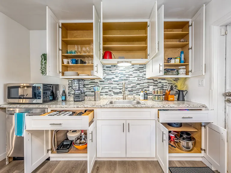 Speckled countertop, adorned with modern appliances like a microwave and a blender, along with neatly placed cooking essentials in the main house kitchen.