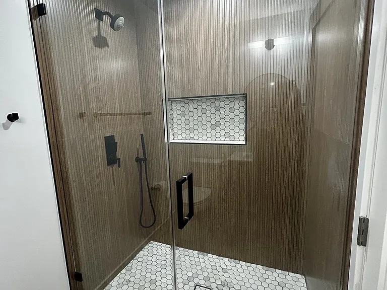 Spa inspired bathroom featuring a large custom walk-in shower with both a rainfall showerhead and a handheld sprayer, framless glass, designer tile, and matte black fixtures.