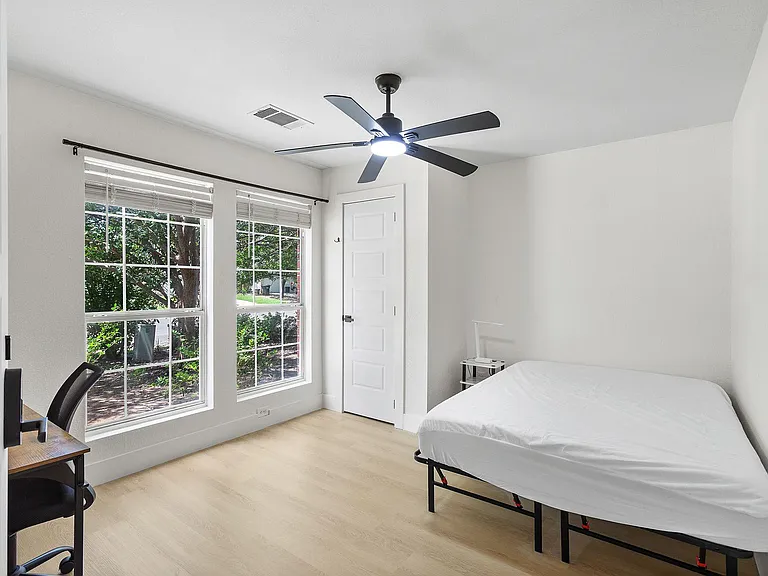 Bedroom with two large windows, ceiling fan, and space for a bed plus a small desk or seating area.