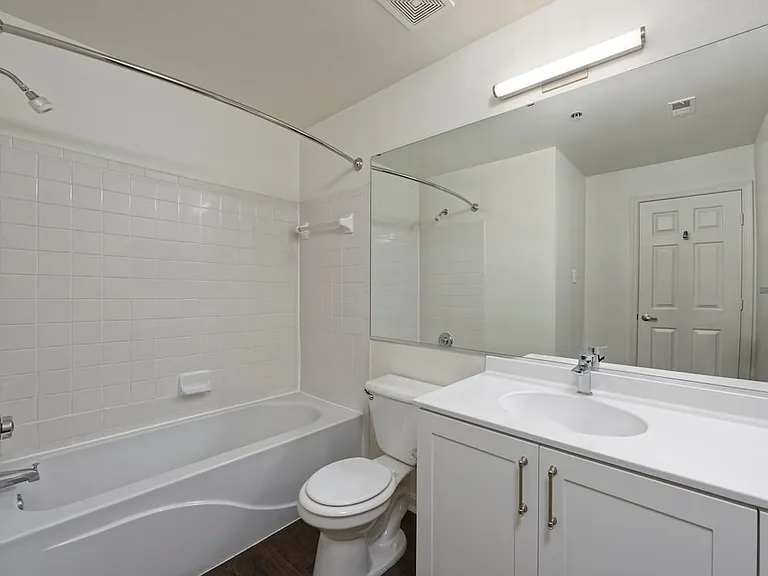 Renovated Package II bath with white cultured marble countertops, white cabinetry, and hard surface flooring