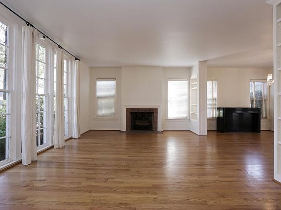 Living room with hardwood floors, floor to ceiling paned windows, fireplace, and built-in bookshelves.