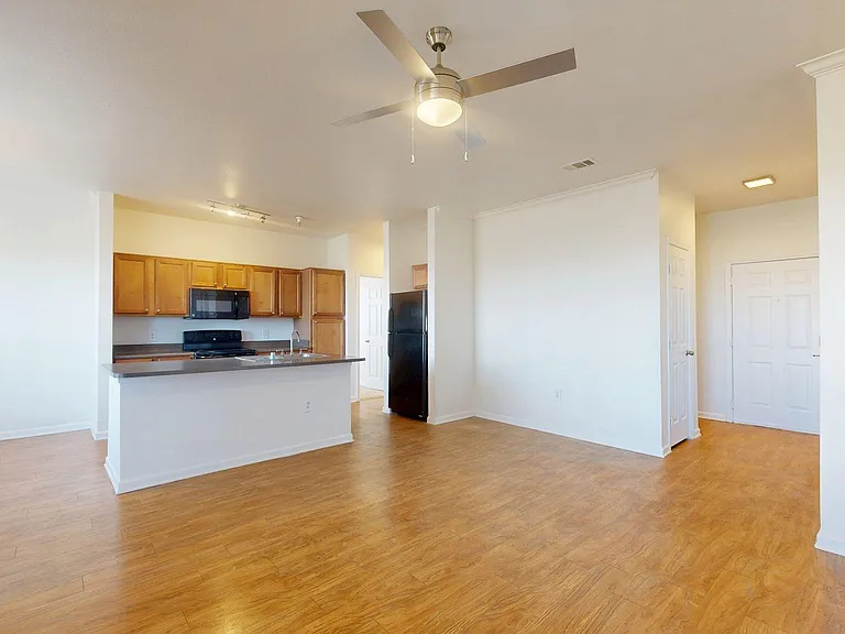 Apartment kitchen, dining room, and living room with plush carpet flooring.