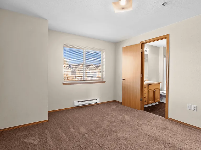 Spacious bedroom with plush carpeting, large window views, and convenient en-suite bathroom access. Spacious bedroom with plush carpeting, large window views, and convenient en-suite bathroom access.