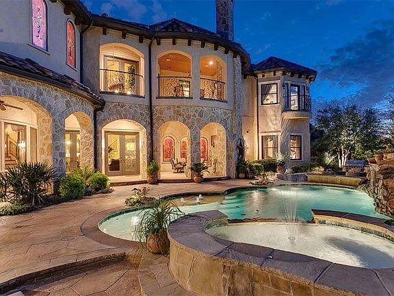 Evening view of back of the home.  Concrete stucco and rock exterior with tile roof.  Large second level patio overlook the back.