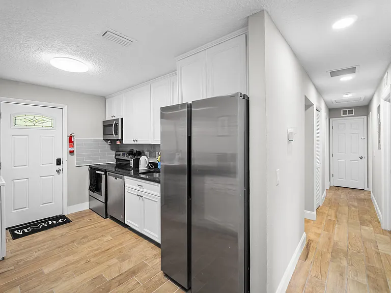 Efficient galley kitchen with stainless appliances, ample white cabinetry, and durable tile flooring off the main hallway.