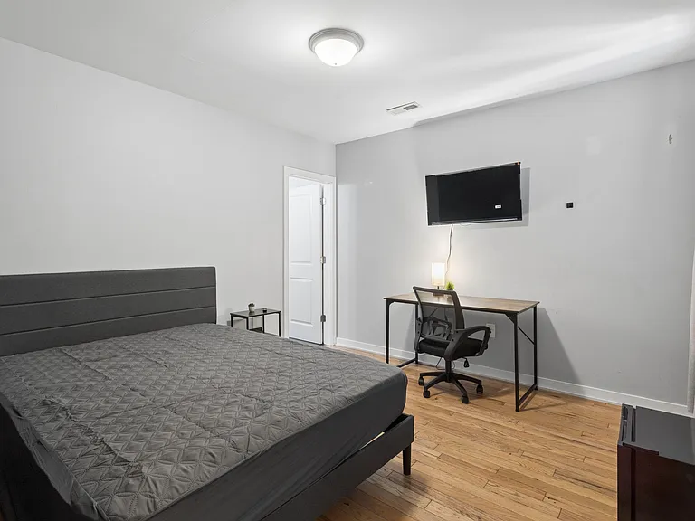 Furnished bedroom with hardwood floors, a work desk and chair, and a wall-mounted TV for easy everyday living.