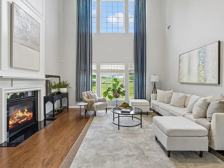 Soaring two-story ceilings, walls of windows, and serene backyard views create a breathtaking great room that feels both grand and inviting-the perfect place to gather, entertain, or simply relax by the fire.