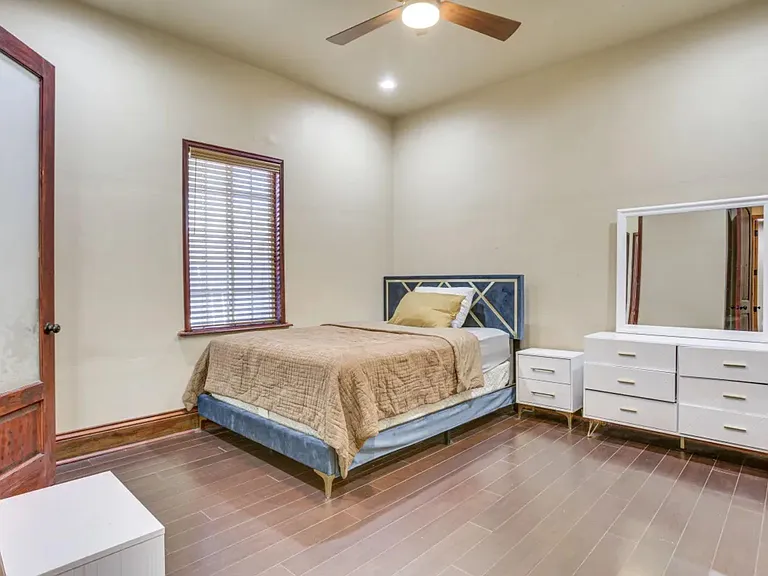 Furnished bedroom with a ceiling fan, window blinds, and wood-look floors, plus a dresser with mirror and nightstand.