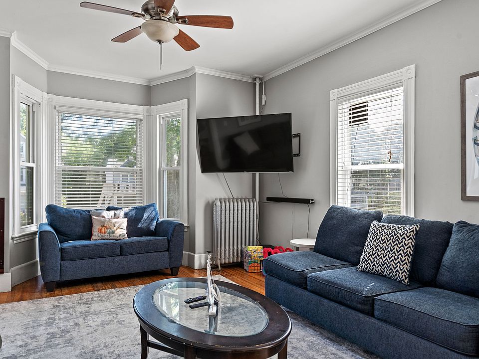 Relax in this bright and comfortable living room, featuring two plush, deep blue sofas providing ample seating for unwinding after a day of exploring. The room boasts a large, wall-mounted Smart TV and an elliptical glass coffee table perfect for games or