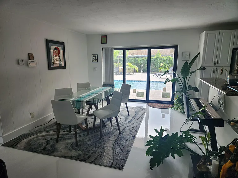 Dining area with a glass-top table and seating for six, opening through sliding doors to a patio and pool view.