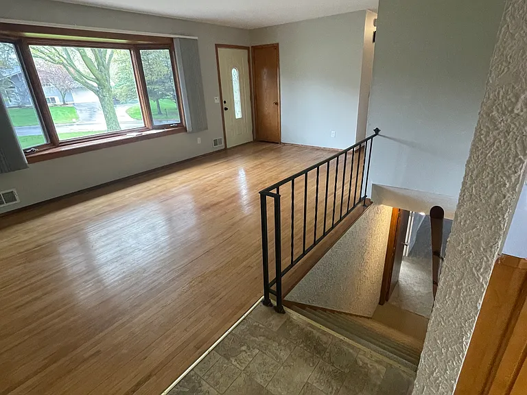 Living room view of front entrance, bay window with blinds, stairway to finished lower level