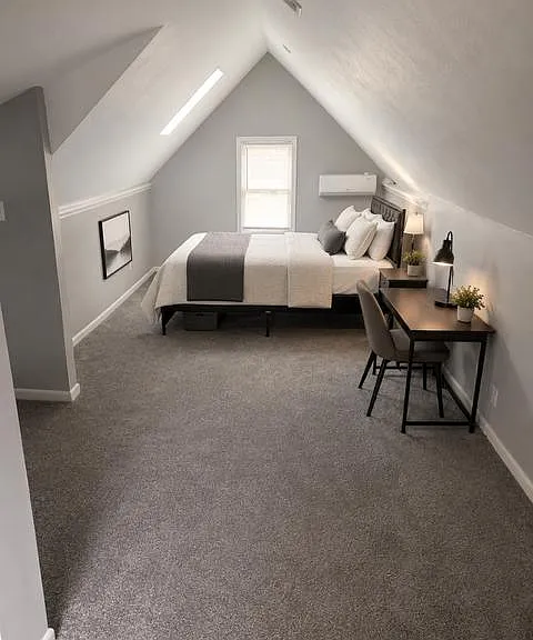 Spacious loft-style bedroom with sloped ceilings, a work desk, and a comfortable bed setup plus natural light from the window