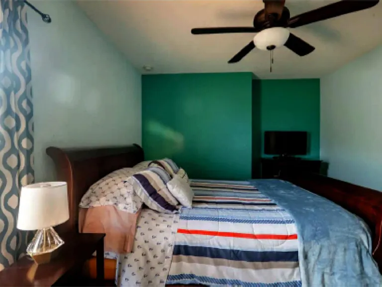 Furnished bedroom featuring a ceiling fan, window with curtains, and space for a dresser or TV setup.