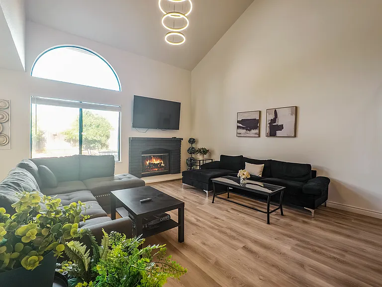 Unwind in the spacious living room featuring soaring ceilings, a modern chandelier, plush seating, a smart TV, and scenic views of the beautifully landscaped backyard.